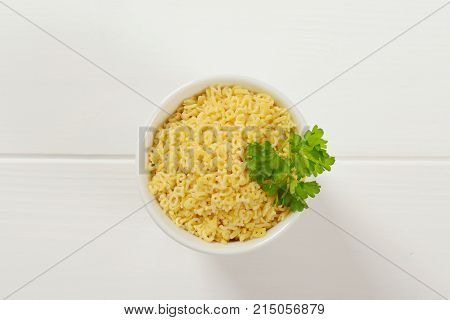 cup of uncooked alphabet pasta on white wooden background