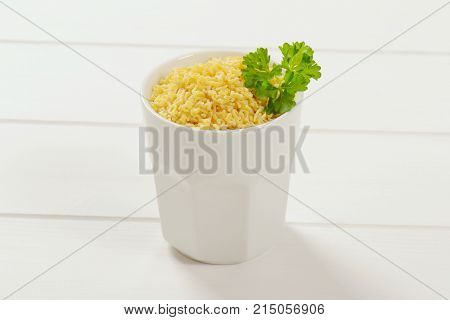 cup of uncooked alphabet pasta on white wooden background