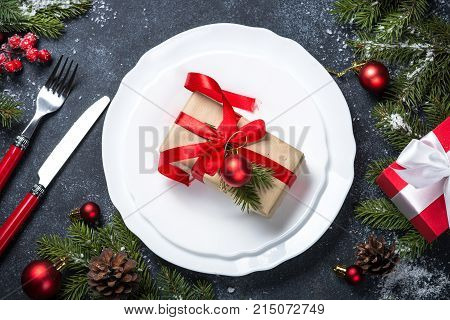 Christmas table setting -white plate cutlary present box with christmas decorations on black stone table. Top view.