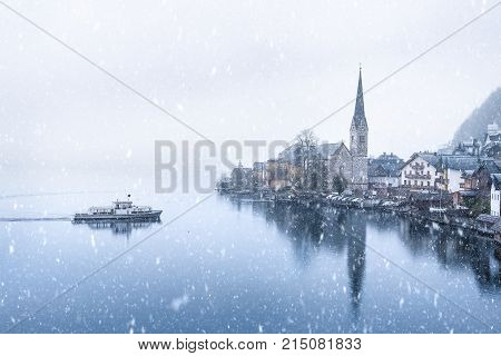 Hallstatt town and a boat under snowfall - Winter weather theme image with the famous touristic town the Hallstatt located on the Hallstatter lakeshore in Austria on a snowy day of November.