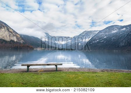 Wooden bench on alpine lake shore - Holiday locations theme image with the Dachstein mountains reflected in the Hallstatter lake water and a wooden bench placed on its shore in Hallstatt Austria.
