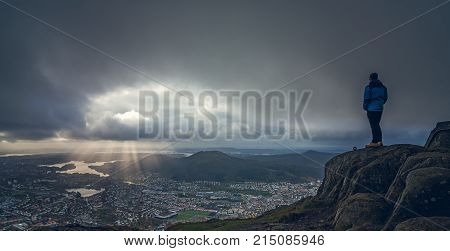 Unidentifiable tourist standing on the top of mount Ulriken in Bergen and looking at the landscape below, Norway