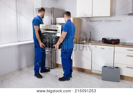Two Young Men In Blue Uniform Fixing Oven In Kitchen