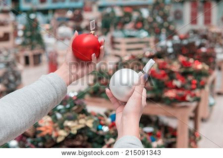 Cheerful happy customer girl choosing Christmas tree decoration balls. difficult decision. Various choice