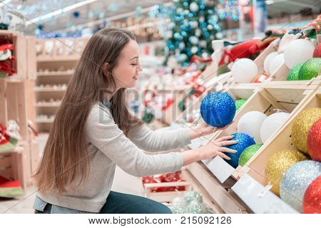 Cheerful happy customer girl choosing Christmas tree decoration balls. difficult decision. Various choice