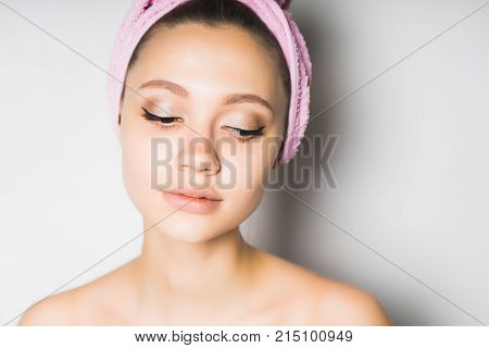 beautiful young girl with clean skin, with a pink towel on her head, looks down