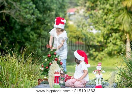 outdoor portrait of two child girls with chritmas tree in green park, christmas in summer, xmas in park