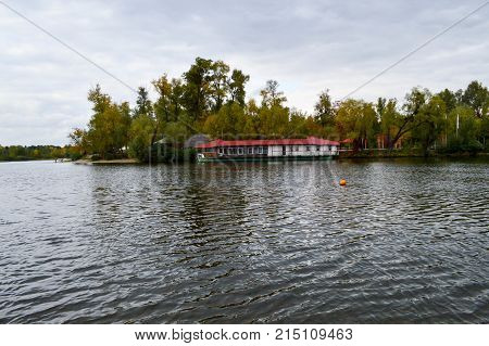 A long boathouse with a red roof on the shore of the lake.