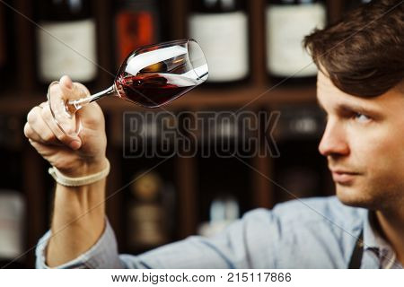 Bokal of red wine on background of male sommelier appreciating color, quality, flavor and sediments of drink. Professional degustation expert in winemaking.