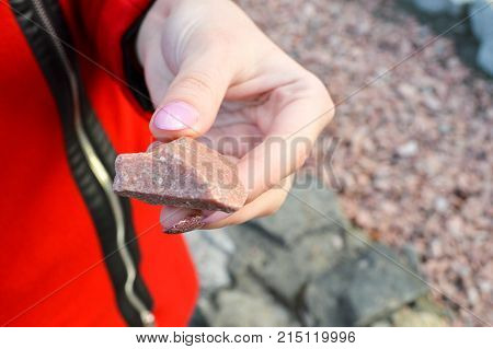 girl with a beautiful manicure holds in her hand a red stone granite