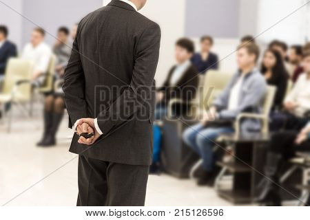 a man in a suit and with an electronic pointer in his hands behind his back speaking in front of an audience.