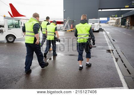 Rear View Of Male Workers Walking On Wet Runway