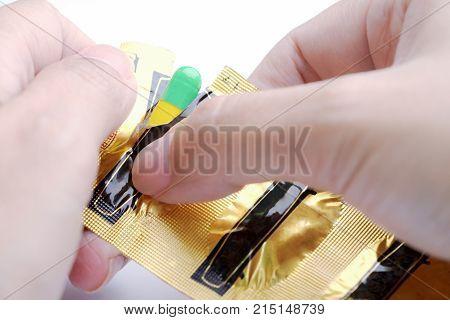 Hands tearing blister pack of green and yellow capsule medical pill.