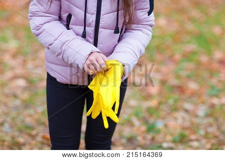 Close-up of a girl in a pink jacket dresses yellow gloves, for cleaning in an autumn park.