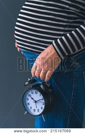 Pregnant female with vintage alarm clock expecting baby in third trimester of pregnancy