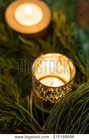 nature, winter, decor concept. close up of small burning candles in different holders with silver dots, that shine like stars, both of them are hiden among the fuzzy spruce needles
