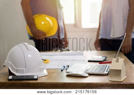 focus at safty helmet on working desk and two engineer standing and dicuss background