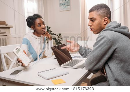 Woman Showing Calculator To Man With Laptop