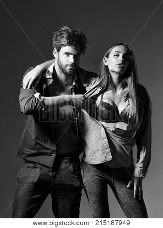 Young sexy couple of pretty girl or beautiful woman in red sexi bra and handsome man muscular macho in unbutton shirts on grey wall