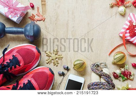 Fitness healthy and active lifestyles love concept dumbbells sport shoes skipping rope or jump rope and smart phone with Christmas decoration items on wood background. Working Out Merry Christmas concept.