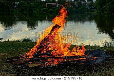 a large fire on the shore of the lake at dusk