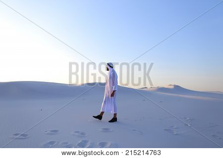 Handsome young Muslim driving along bottomless desert and looking toward sunset, admiring beauty of nature on warm clear night. attractive Muslim smiles widely and spreads hands to sides, straightens clothes in wind and whirls around, delighted by breadth