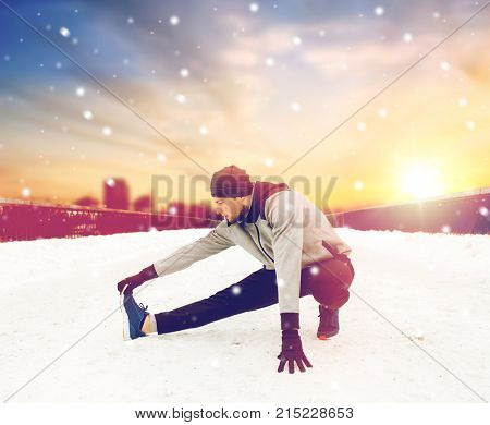 fitness, sport, people, exercising and healthy lifestyle concept - young man stretching leg and warmig up on snow covered winter bridge
