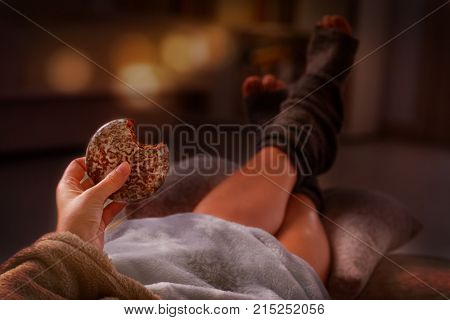 Woman with sweet gingerbread cookie and feet lying on pilow in the cozy room