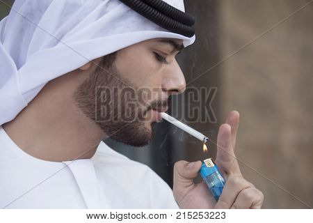 Close-up of a Arab young man wearing kandoura and agal lighting a cigarette.