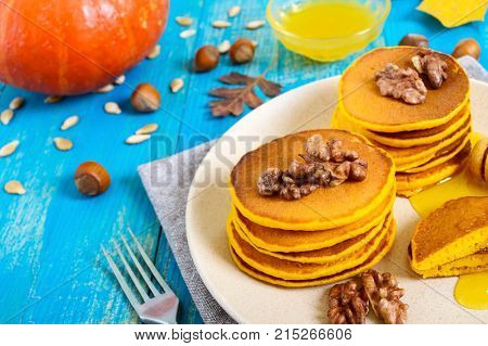 Fragrant golden pumpkin pancakes with honey and walnuts on a blue wooden background. Traditional American dish