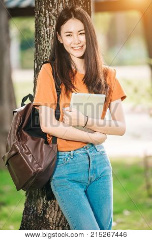 A young or teen asian girl student in university smiling and reading the book and look at the tablet or labtop computer in summer holiday.