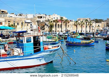 MARSAXLOKK, MALTA - APRIL 1, 2017 - Traditional Maltese Dghajsa fishing boats in the harbour with waterfront buildings to the rear Marsaxlokk Malta Europe, April 1, 2017.
