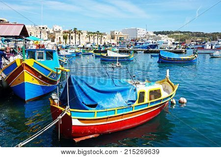 MARSAXLOKK, MALTA - APRIL 1, 2017 - Traditional Maltese Dghajsa fishing boats in the harbour with waterfront buildings to the rear Marsaxlokk Malta Europe, April 1, 2017.