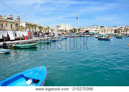 MARSAXLOKK, MALTA - APRIL 1, 2017 - Traditional Maltese Dghajsa fishing boats in the harbour with waterfront buildings and market stalls to the rear Marsaxlokk Malta Europe, April 1, 2017.