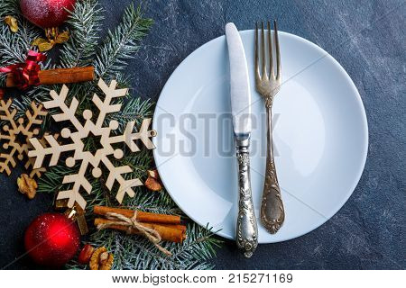 White round plate with a table knife and fork, next to a branch of a Christmas tree decorated with Christmas decorations.