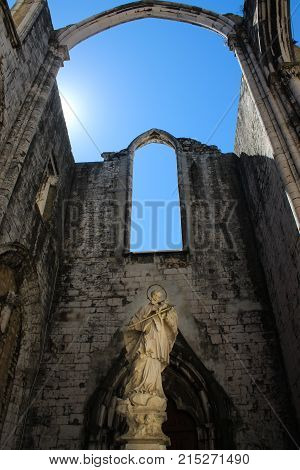 A religious statue stands under blue skys in the ruins of the catherdal at Carmo Convent. Lisbon Portugal.