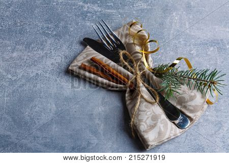 On the shabby surface, the fork and knife in the napkin are decorated with a Christmas tree and cinnamon sticks. Against the background is a layout with a place for an inscription. View from above. Indoors.
