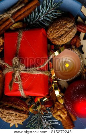 A close-up small red gift box, a burning candle, a walnut, cinnamon sticks and christmas balls. Christmas decor. View from above. Indoors.