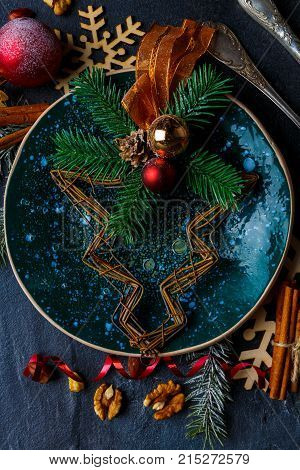 On top of the beautiful round plate with dark green glossy surface is a creative Christmas tree with balls, a cone and ribbon. View from above. Close-up. Indoors.