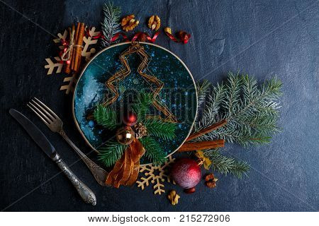 Decorative Christmas tree with a barbed branch and balls on a glossy plate, next to old cutlery.