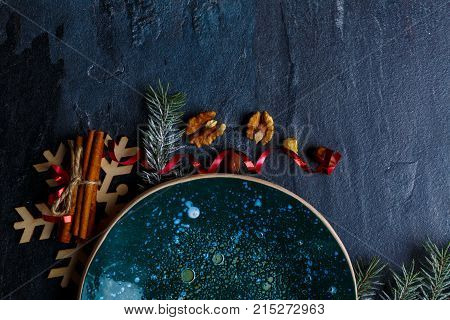 On a dark surface a glossy dark board of round shape and decorations from twigs of a Christmas tree, wooden snowflakes and cinnamon sticks. Place for the inscription. View from above.