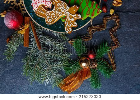 On a dark surface, Christmas decorations of spiny twigs of Christmas trees, wooden snowflakes and cinnamon sticks and sweet Christmas gingerbread. View from above.