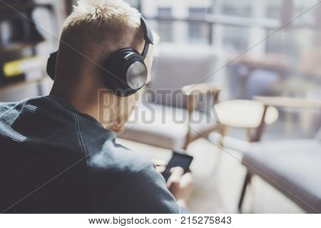 Attractive young man wearing glasses casual clothes.Man sitting in vintage armchair modern loft studio and relaxing whith headphone music. Blurred background.Horizontal