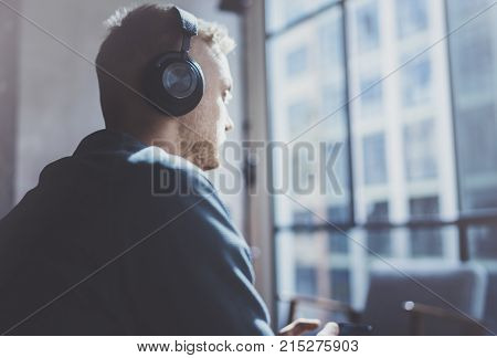 Attractive young man wearing glasses casual clothes.Man sitting in vintage armchair modern loft studio and relaxing whith headphone music. Blurred background.Horizontal