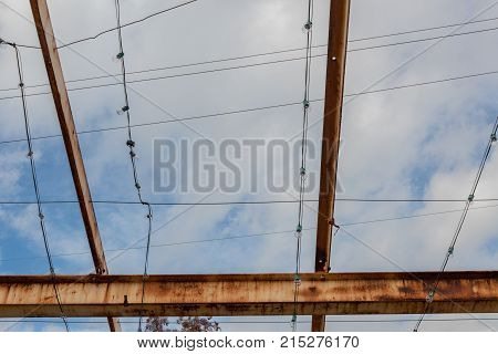 Gridwork of overhead beams painted and rusted against a blue sky horizontal aspect