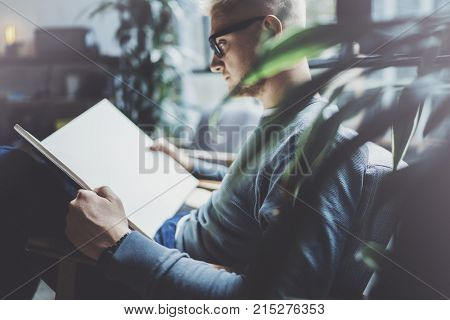 Portrait handsome young man wearing glasses casual clothes holding book hands.Man sitting in vintage armchair modern loft studio reading book. Blurred background.Horizontal