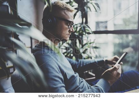 Attractive young man wearing glasses casual clothes.Man sitting in vintage armchair modern loft studio and relaxing whith headphone music. Blurred background.Horizontal