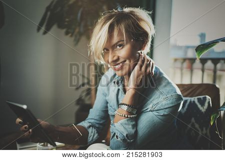 Smiling young woman wearing casual clothes and using electronic device while spending relax time in vacation travel.Attractive woman owner communicating on digital tablet.Blurred background