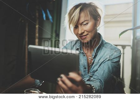 Smiling young woman wearing casual clothes and using electronic device while spending relax time in vacation travel.Attractive woman owner communicating on digital tablet.Blurred background