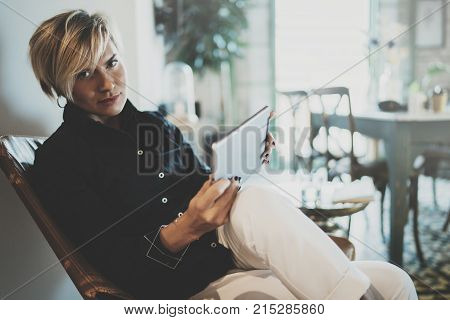 Smiling young woman wearing casual clothes and using electronic device while spending relax time in vacation travel.Attractive woman owner communicating on digital tablet.Blurred background